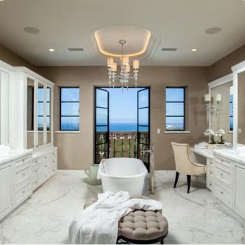 Luxurious bathroom featuring Euroline Steel Windows and Steel Swing Doors, with tall steel-framed windows providing a breathtaking ocean view, complemented by elegant furnishings including a standalone bathtub, vanity areas, and a plush ottoman under a modern chandelier.