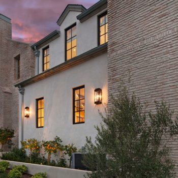 Twilight view of an elegant home facade featuring Euroline Steel Casement Windows, with tall, narrow windows set in a textured brick wall, accented by warm outdoor lanterns that enhance the romantic and welcoming atmosphere of the landscaped entryway.