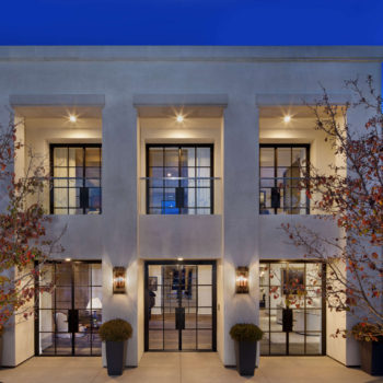 Modern, two-story building with Euroline Steel Windows and Doors, featuring elegant swing doors on the ground floor. The facade is illuminated by warm lighting, with trees on either side enhancing the architectural beauty.