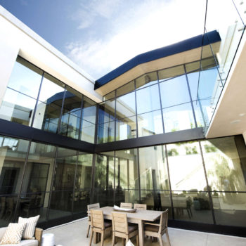 Contemporary patio area enhanced by Euroline Steel Curtain Wall Windows, featuring a large, curved glass facade with black steel frames that connect seamlessly to the building’s modern structure. This architectural design allows for ample natural light and integrates indoor comfort with outdoor living.
