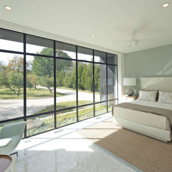Modern bedroom enhanced by Euroline Steel Curtain Wall Windows, featuring floor-to-ceiling black steel frames that offer expansive views of a serene outdoor landscape. The room combines sleek design with comfort, highlighted by a large bed and minimalist furniture.