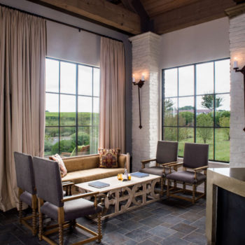 Rustic lounge area outfitted with Euroline Steel Curtain Wall Windows, allowing for unobstructed views of the vineyard outside. The space features elegant drapery, exposed brick walls, and comfortable seating, enhancing the cozy, natural ambiance.