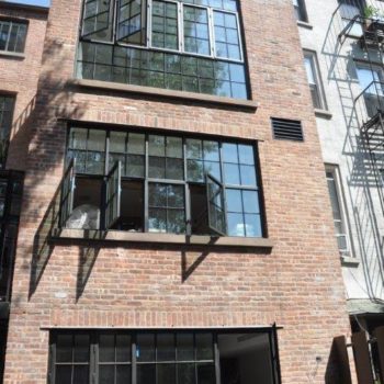 Urban apartment building featuring Euroline Steel Casement Windows, with large black steel-framed windows enhancing the vintage red brick facade. The design incorporates an industrial aesthetic with modern touches, providing ample natural light and urban charm.